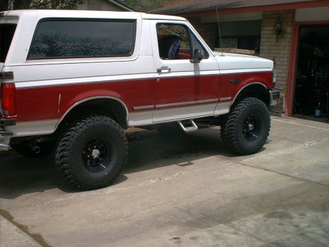 1994 Ford Bronco - Side view of a red and white Ford Bronco with aftermarket wheels and tires.