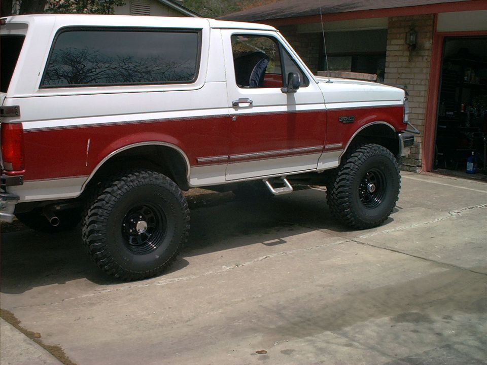 White and red lifted Ford Bronco on black wheels, side view in driveway