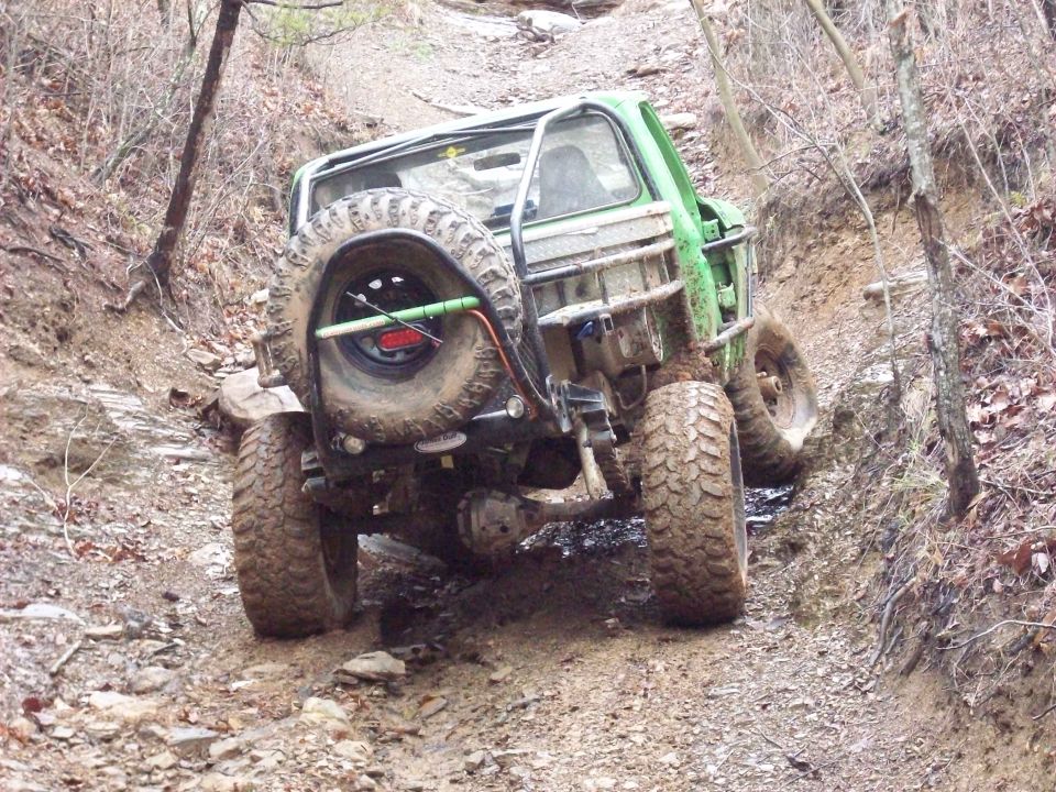 Green off-road vehicle with a spare tire mounted on the back, driving on a muddy trail