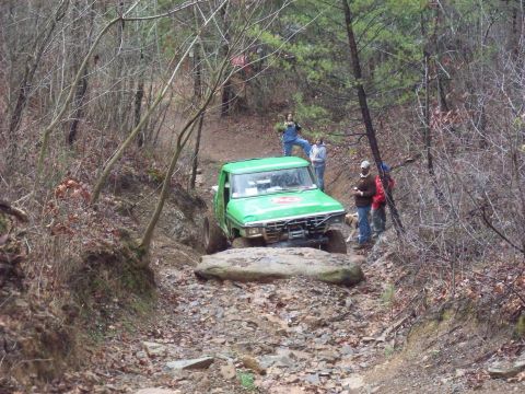 1978 Ford Bronco - A green off-road truck carefully maneuvers over a large rock on a challenging trail.