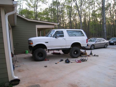 1996 Ford Bronco - A lifted 1996 Ford Bronco is parked outside a garage, with other vehicles visible in the background.