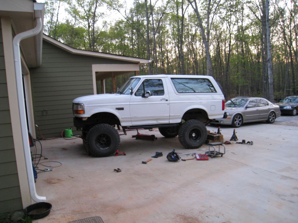 White 1996 Ford Bronco lifted with large tires, parked outside a garage