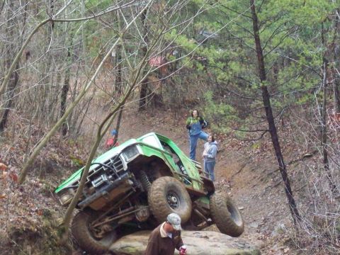 1978 Ford Bronco - A modified green truck navigates a rocky incline in a wooded area.