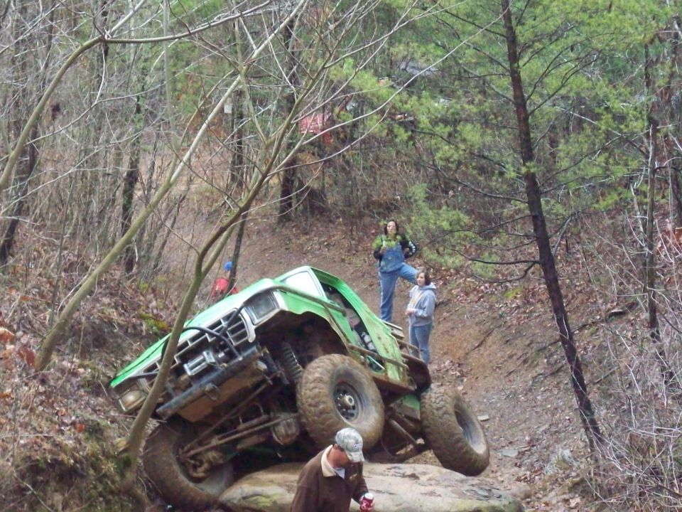 Green off-road truck tilted on rocks with people watching