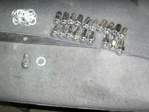 1987 Ford Bronco - A collection of lug nuts and washers are laid out on a dark, textured surface.