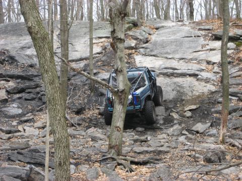 1991 Ford Bronco - This modified SUV navigates a challenging rocky terrain in a wooded area.