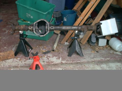1994 Ford Bronco - A Dana 44 axle assembly is supported by jack stands, with various storage bins and wooden debris in the background.