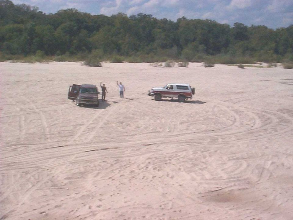 Bronco and van parked on sand, two people standing near van