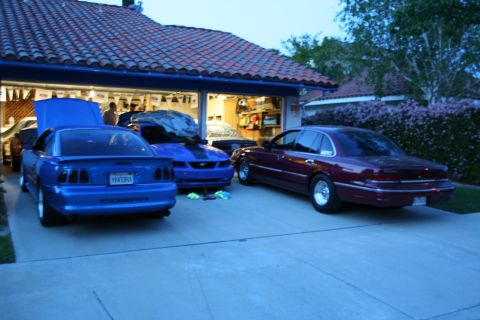 1992 Ford Crown Victoria - Three cars are parked in a driveway in front of an open garage. The maroon sedan is on the right.