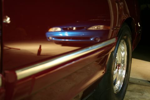 1992 Ford Crown Victoria - The reflection shows a blue car's front end, including headlights and grille, in the polished side of a red vehicle.