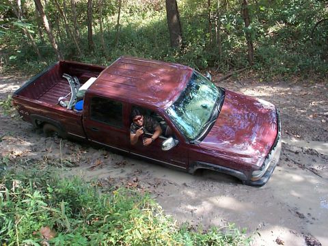 1994 Ford Bronco - A maroon pickup truck is stuck in the mud with a driver giving a thumbs up.