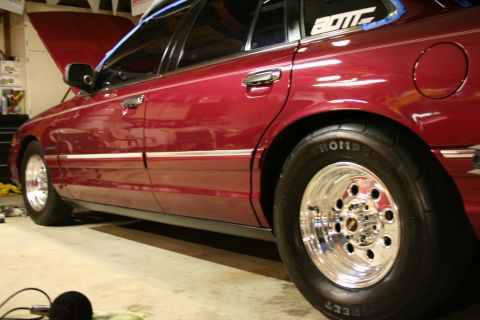 1992 Ford Crown Victoria - The side profile of a red sedan is shown with custom chrome wheels and performance tires, parked indoors.