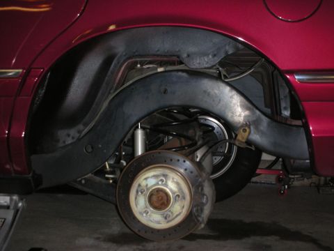 1992 Ford Crown Victoria - The rear suspension and wheel well of a red 1992 Ford Crown Victoria are shown, drilled brake rotors and modified components.