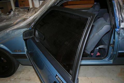 1990 Ford Mustang - Interior view of a blue car with the driver's side door open, showing the seats and the car covered in plastic sheeting.