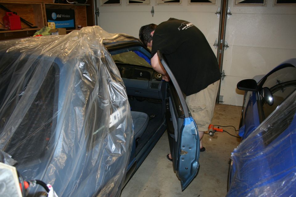 Interior of a car covered in plastic, with a person working on the dashboard