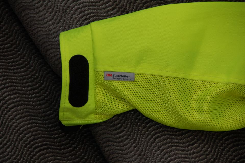 Neon yellow jacket sleeve with 3M Scotchlite reflective material tag and black velcro patch on textured gray background