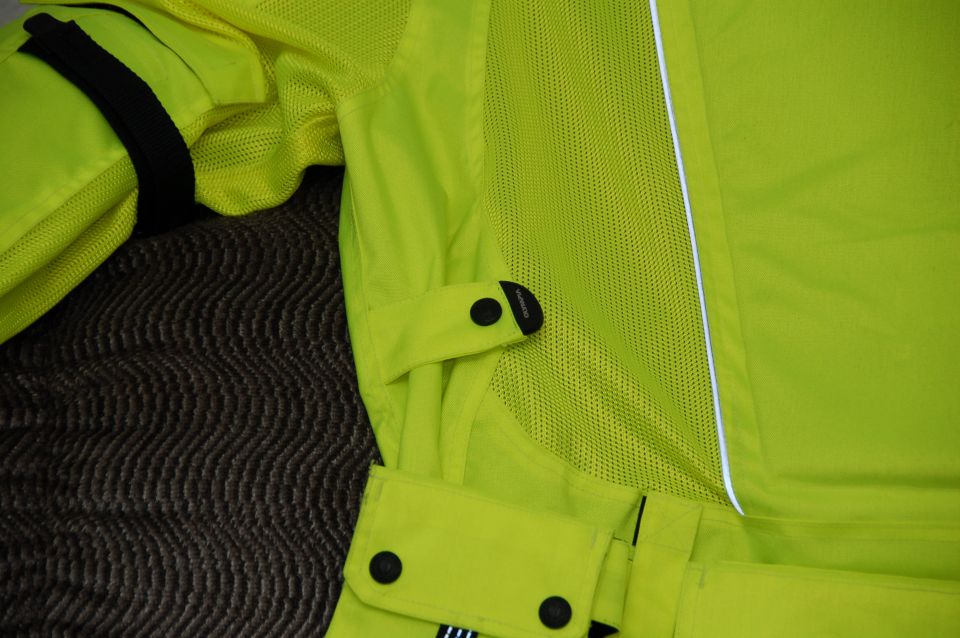 Close-up of bright yellow motorcycle jacket with black snaps and mesh panels. Supermotors.net logo visible