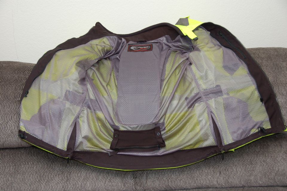 Interior of a dark motorcycle jacket with yellow lining and mesh panels, laid open on a couch