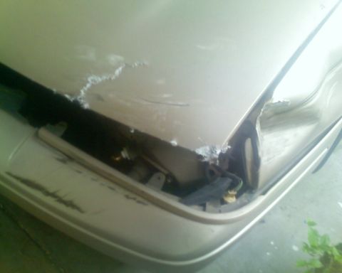 1991 Ford Taurus - Close-up of a damaged tan car's front end, showing a crumpled bumper and hood.