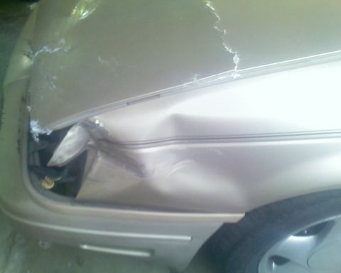 1991 Ford Taurus - Front passenger side of a 1991 Ford Taurus with significant damage to the fender and hood.