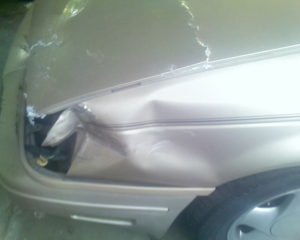 1991 Ford Taurus front fender and hood damaged, showing crumpled metal and cracked paint
