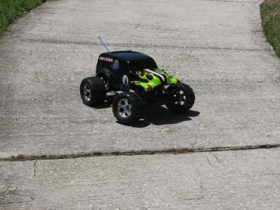 RC monster truck with green flames and 'Grave Digger' text on side, parked on a concrete path