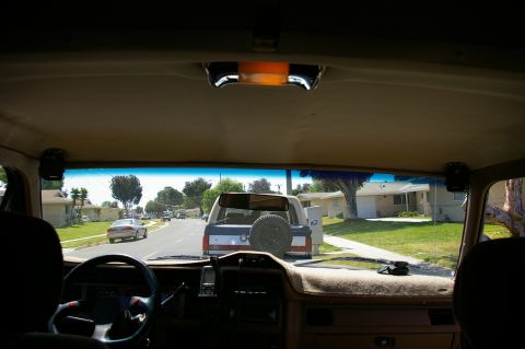 1986 Ford Bronco - View from inside a Ford Bronco shows a suburban street with a silver sedan and a white Bronco ahead.