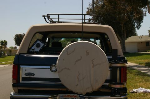 1986 Ford Bronco - Rear view of a Ford Bronco with a spare tire cover and roof rack, parked in a residential area.