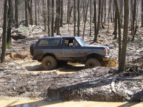 1991 Ford Bronco - Ford Bronco navigates a challenging muddy trail in a forest setting.