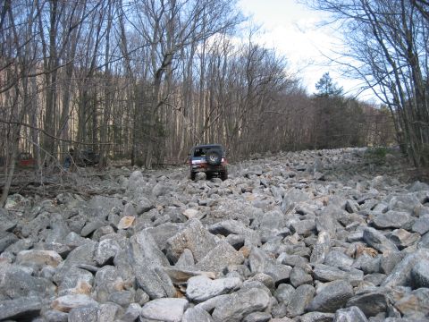 1991 Ford Bronco - An SUV tackles a challenging rocky terrain in a forest during a meet and greet event.