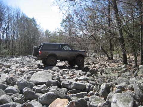 1991 Ford Bronco - A Ford Bronco navigates a rocky trail through a forest.