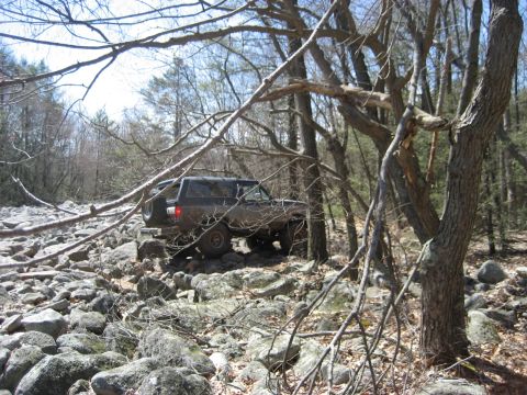 1991 Ford Bronco - A 1991 Ford Bronco navigates a challenging rocky terrain in a wooded area.