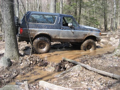 1991 Ford Bronco - A blue and silver 1991 Ford Bronco tackles a challenging muddy off-road course.
