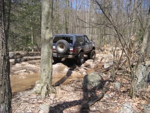 1991 Ford Bronco - Ford Bronco tackling a challenging off-road course with mud and rocks.