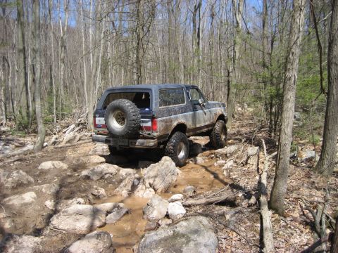 1991 Ford Bronco - A Ford Bronco navigates a challenging off-road course with mud and rocks.