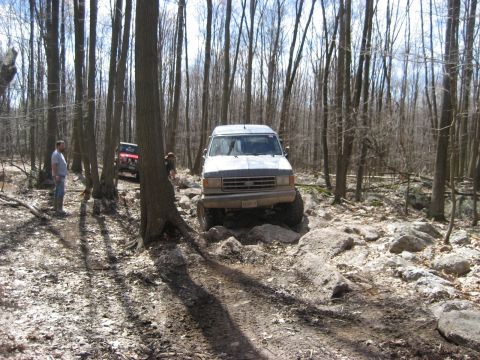 1991 Ford Bronco - 1991 Ford Bronco tackling a challenging rocky path in a forest setting with another vehicle present.