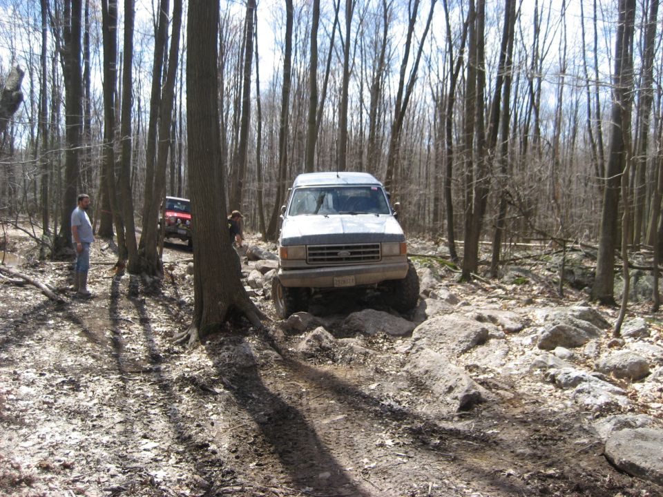 1991 Ford Bronco navigating rocks on a wooded trail, another SUV behind it