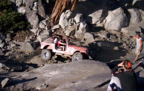 1989 Ford Bronco - A red off-road vehicle tackles a challenging rocky trail with people watching.