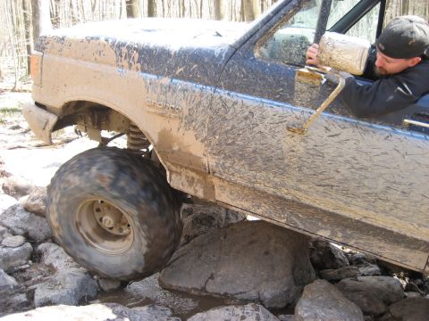 1991 Ford Bronco - 1991 Ford Bronco tackling a rocky off-road obstacle with a driver at the wheel.