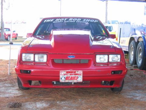 1992 Ford Mustang - Front view of a red Ford Mustang with a prominent hood scoop and "The Hot Rod Shop" banner.