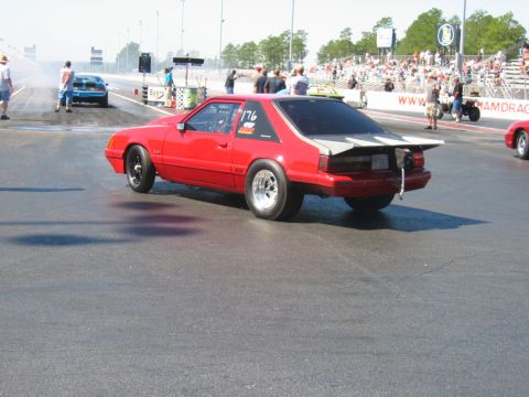 1992 Ford Mustang - A red 1992 Ford Mustang drag car is seen on the track, with racing numbers visible on its door.