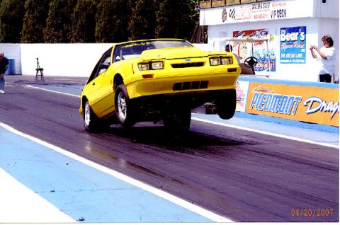 1992 Ford Mustang - A yellow Fox body Mustang launches with its front wheels off the ground at a drag strip.