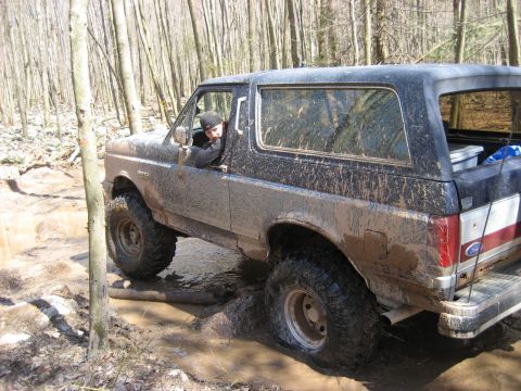 1991 Ford Bronco - A Ford Bronco navigates a muddy path in a forest, with its tires deep in the muck.