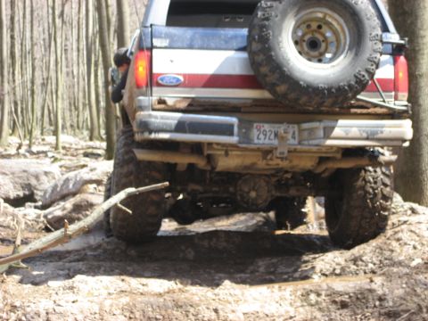 1991 Ford Bronco - This Ford Bronco is navigating a challenging off-road trail through a forest.