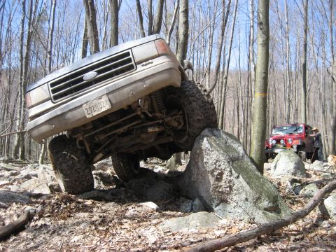 1991 Ford Bronco - 1991 Ford Bronco navigating a rocky obstacle course in a forest setting.
