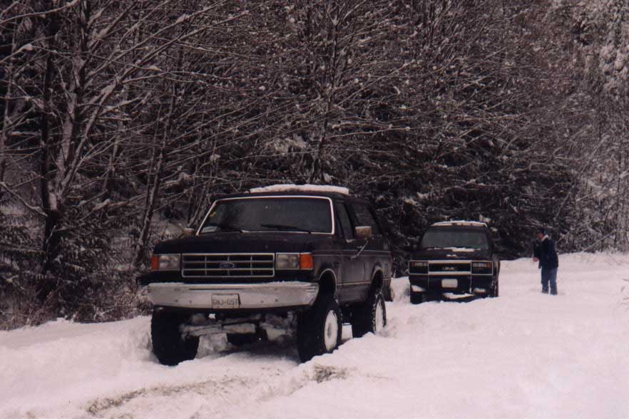 Dark Ford Bronco in snow, another SUV behind it