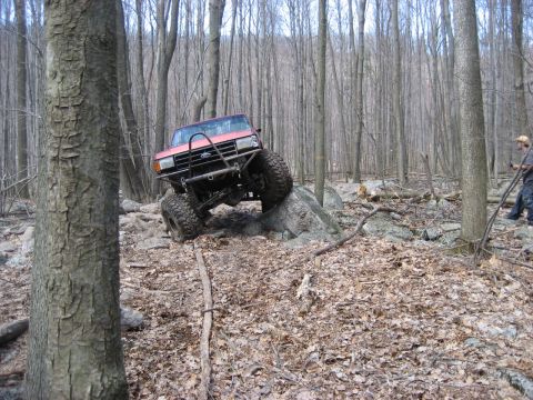 1991 Ford Bronco - This modified truck is navigating a rocky trail through a dense forest.
