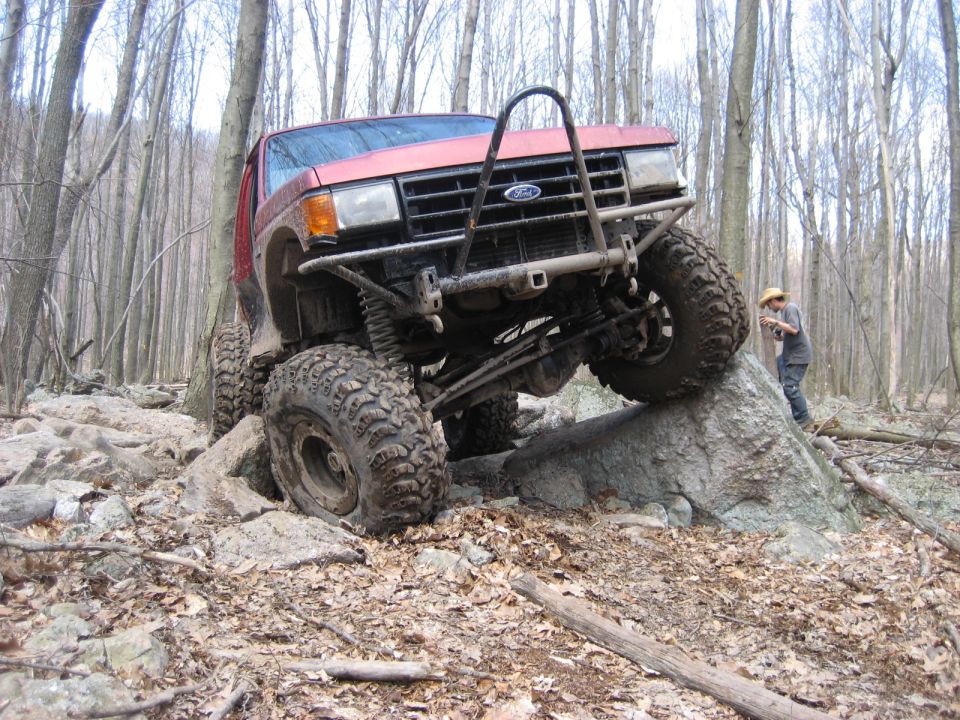 Red off-road SUV with custom bumper climbing large rocks in a forest