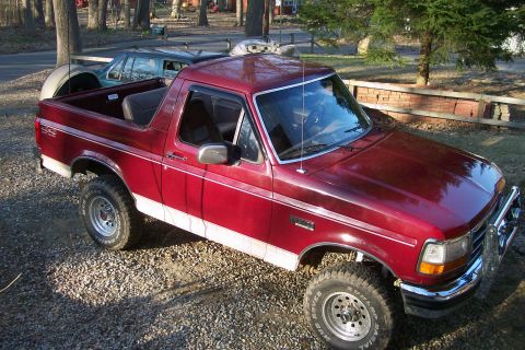 1993 Ford Bronco - A red pickup truck is parked on a gravel surface with another vehicle in the background.
