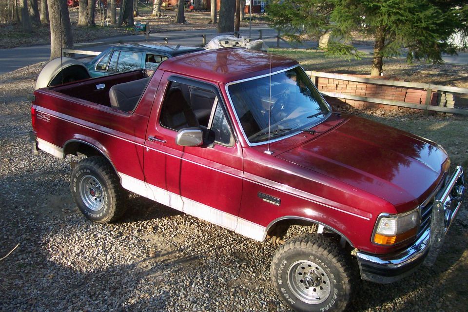 red pickup truck with white trim, spare tire on back, parked on gravel